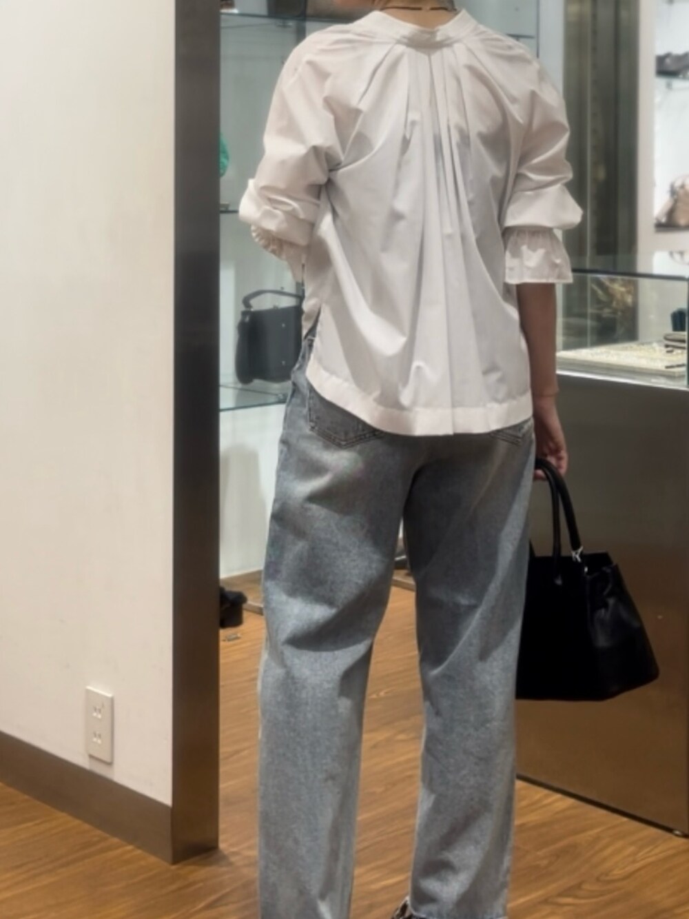 ブラック系のハンドバッグ、ブラック系のパンプス、ブルー系のデニムパンツを着用したレディースの秋コーディネートの5枚目の写真