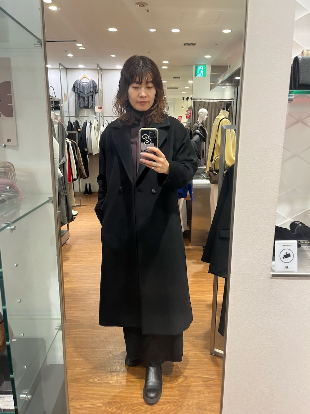 ブラック系のチェスターコート、レッド系のシャツ/ブラウス、ゴールド系のピアス（両耳用）を着用したレディースの冬コーディネートの2枚目の写真