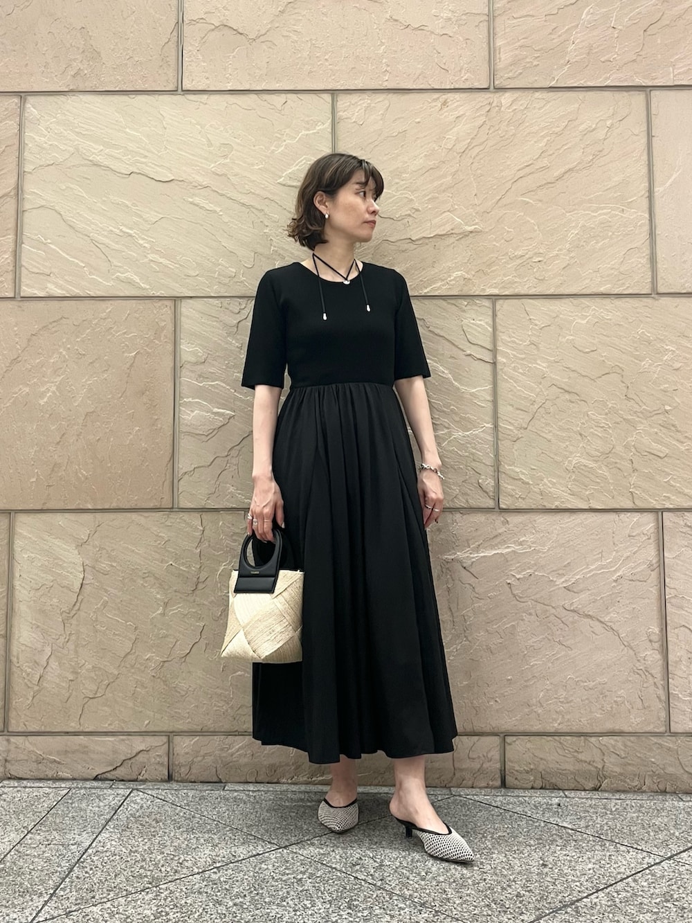 ブラック系のワンピース、ベージュ系のショルダーバッグ、ブラック系のパンプスを着用したレディースの夏コーディネートの2枚目の写真
