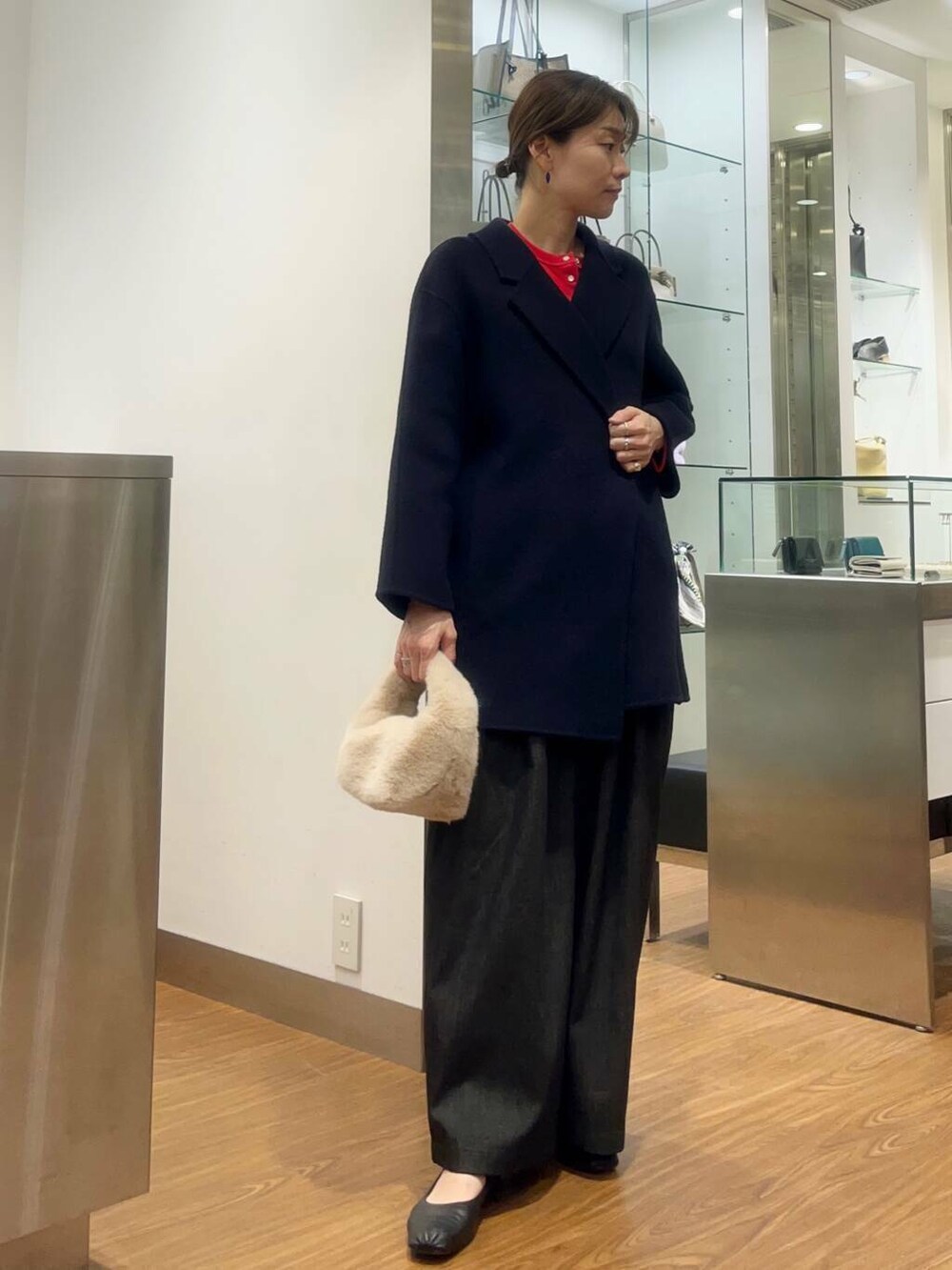 レッド系のカーディガン/ボレロ、ブルー系のチェスターコート、ブラック系のデニムパンツを着用したレディースの秋コーディネートの5枚目の写真