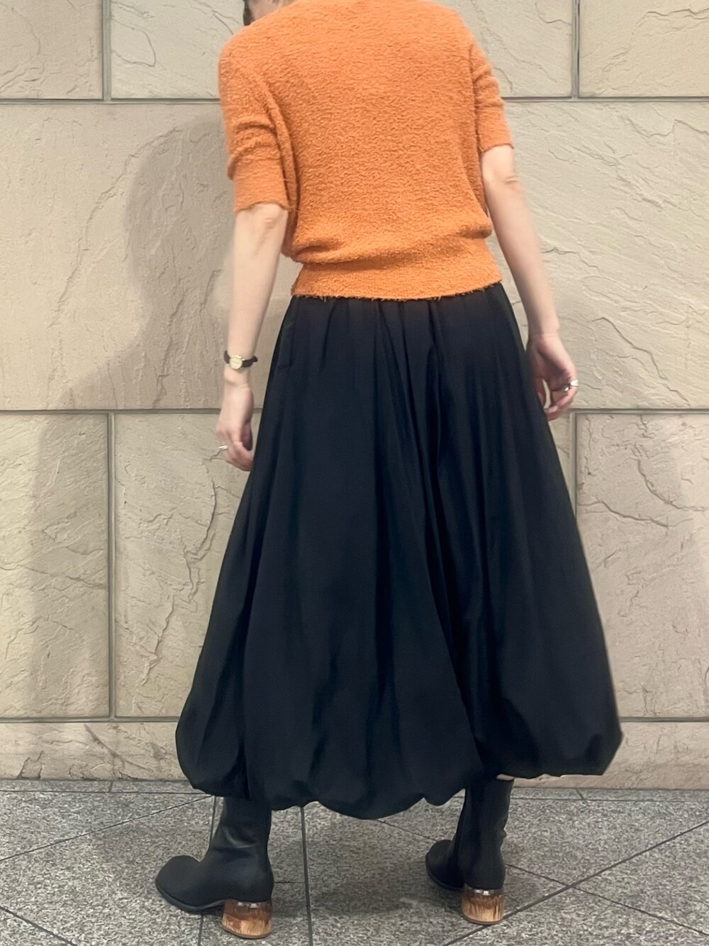 ブラック系のシューズ、ブラック系のスカート、オレンジ系のニット/セーターを着用したレディースの夏コーディネートの2枚目の写真
