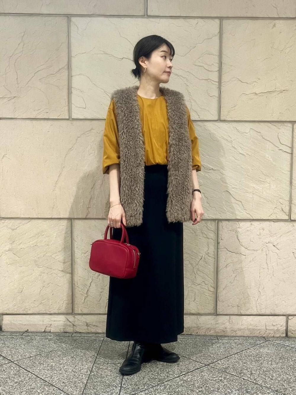 ブラウン系のベスト、オレンジ系のシャツ/ブラウス、ブラック系のスカートを着用したレディースの秋コーディネートの3枚目の写真