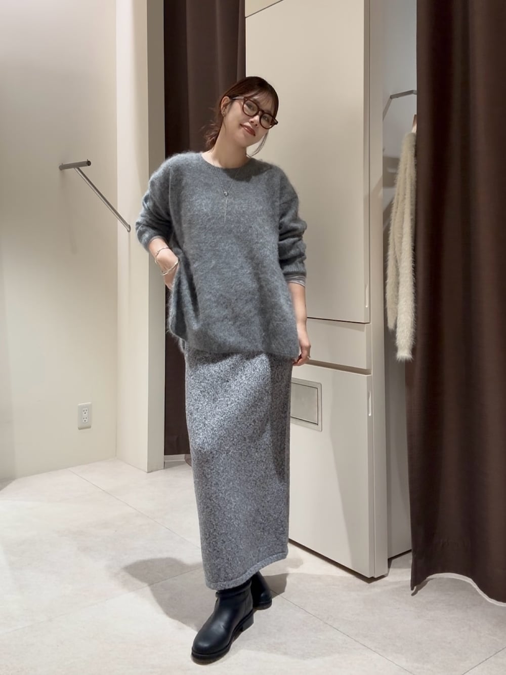 グレー系のニット/セーター、グレー系のスカート、ブラック系のブーツを着用したレディースの秋コーディネートの2枚目の写真