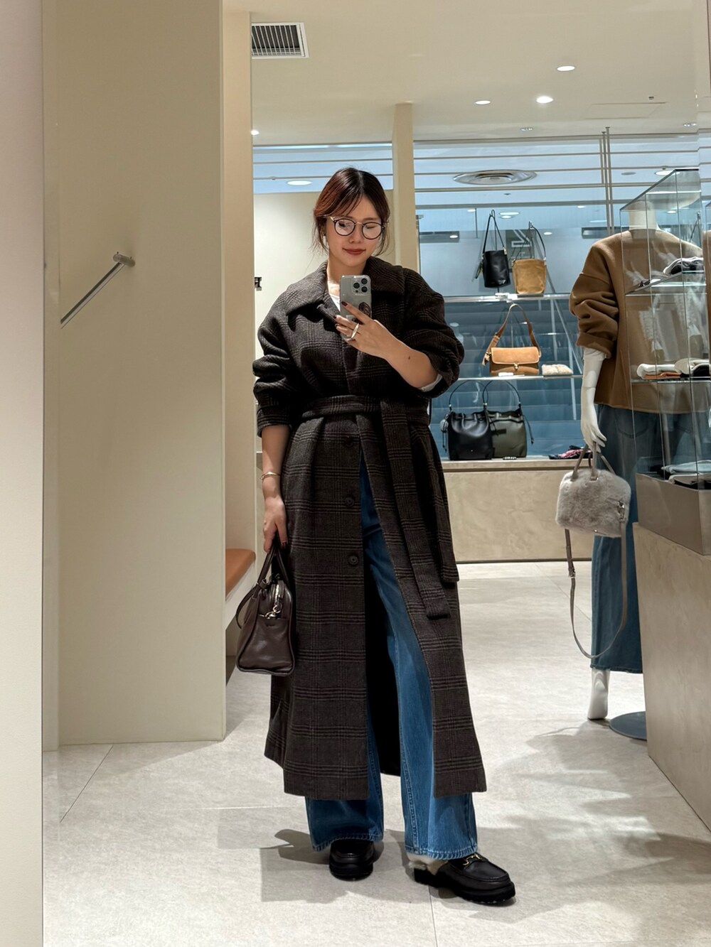 ブラウン系のステンカラーコート、ブルー系のデニムパンツを着用したレディースの秋コーディネートの3枚目の写真