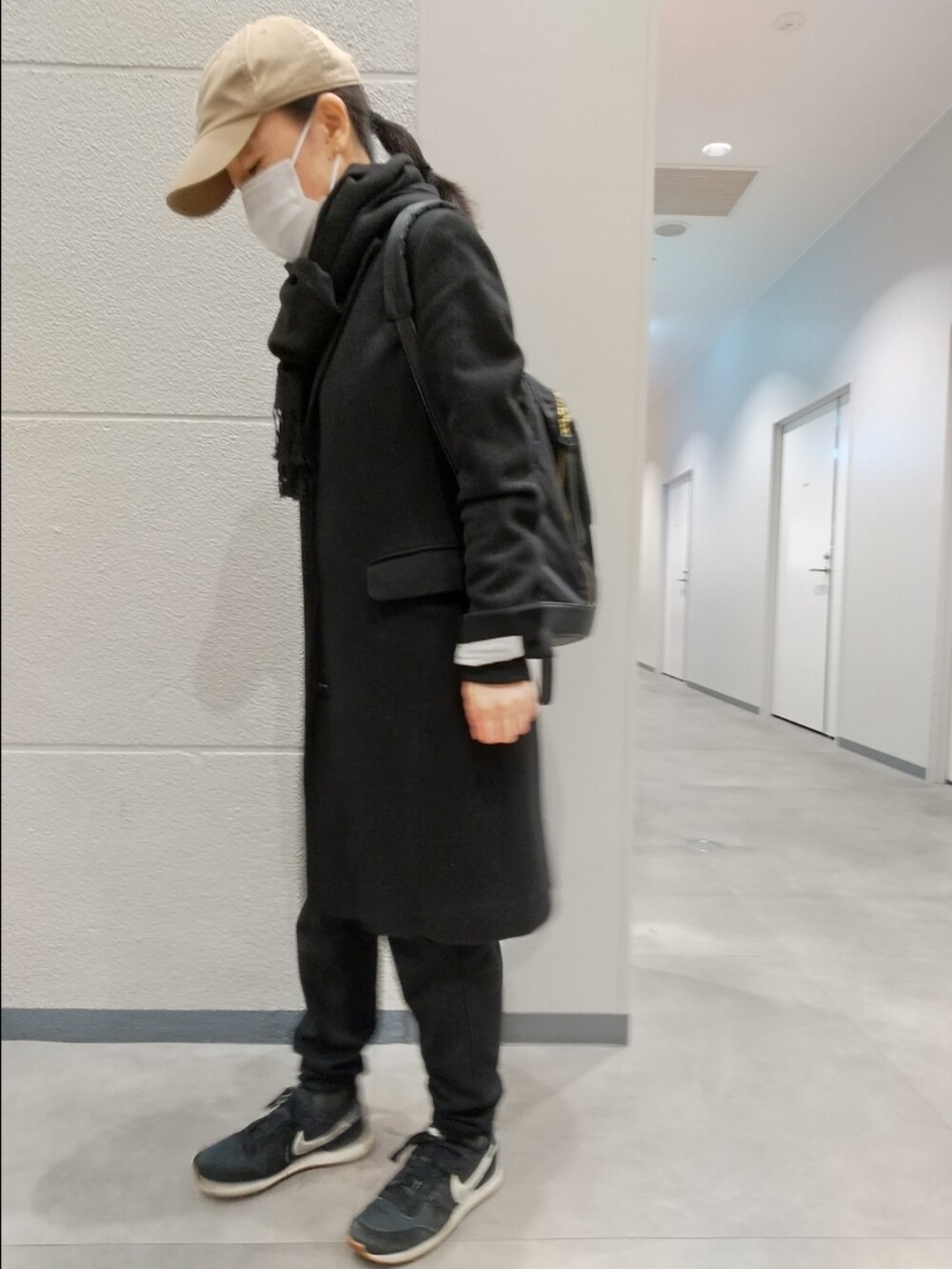 ブラック系のチェスターコート、ブラック系のパンツ、ブラック系のスニーカーを着用したレディースの冬コーディネートの2枚目の写真