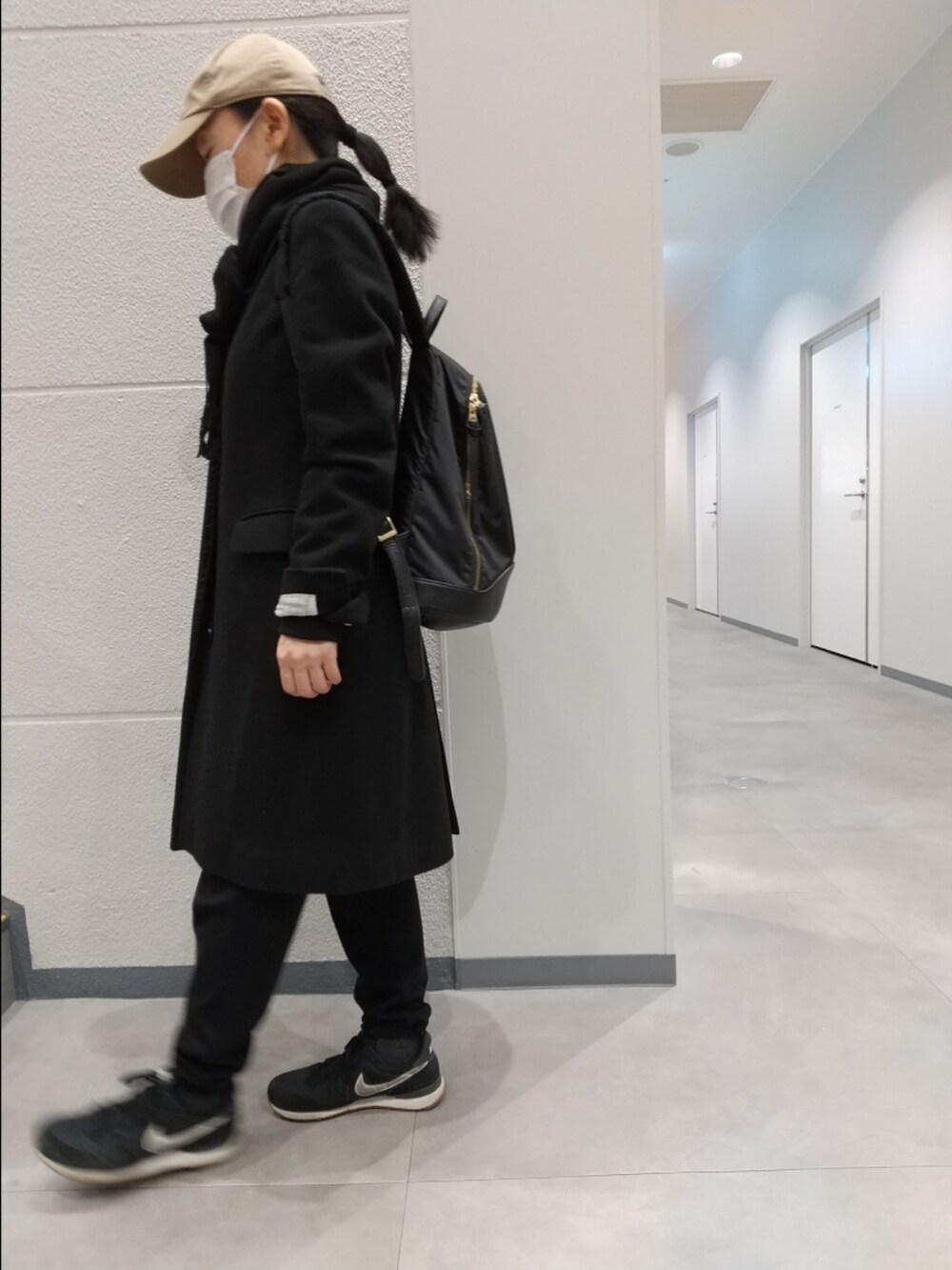 ブラック系のチェスターコート、ブラック系のパンツ、ブラック系のスニーカーを着用したレディースの冬コーディネートの3枚目の写真