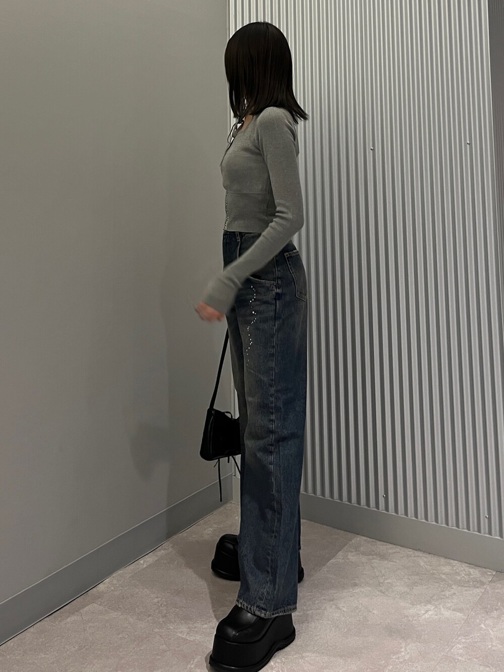 グレー系のニット/セーター、ブルー系のデニムパンツ、ブラック系のショルダーバッグを着用したレディースの秋コーディネートの2枚目の写真
