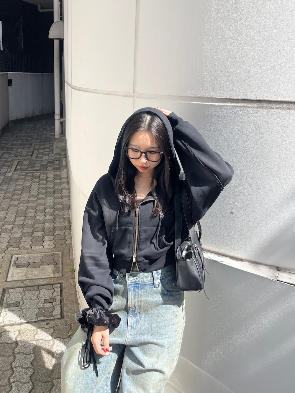 ブラック系のパーカー、ブルー系のデニムパンツ、ブラック系のハンドバッグを着用したレディースの秋コーディネートの4枚目の写真