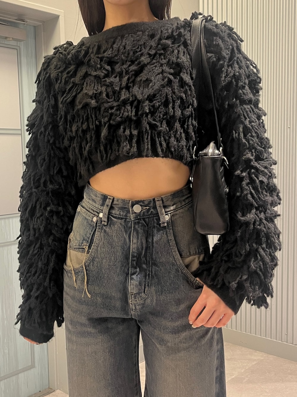 ブルー系のデニムパンツ、ブラック系のニット/セーター、ブラック系のショルダーバッグを着用したレディースの秋コーディネートの4枚目の写真