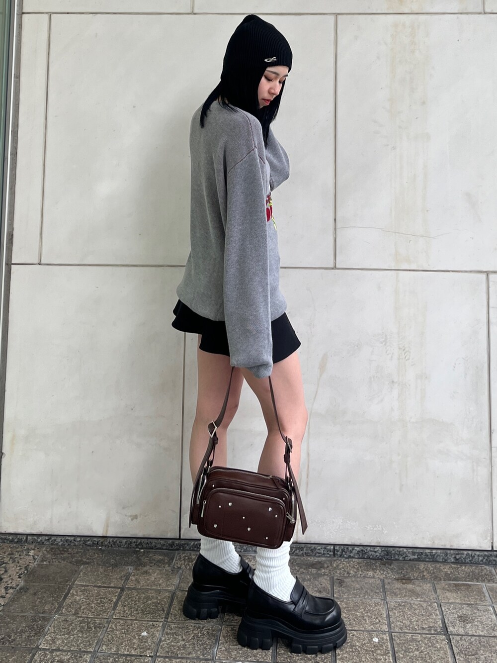 グレー系のニット/セーター、ブラック系のスカート、ブラウン系のショルダーバッグを着用したレディースの春コーディネートの2枚目の写真