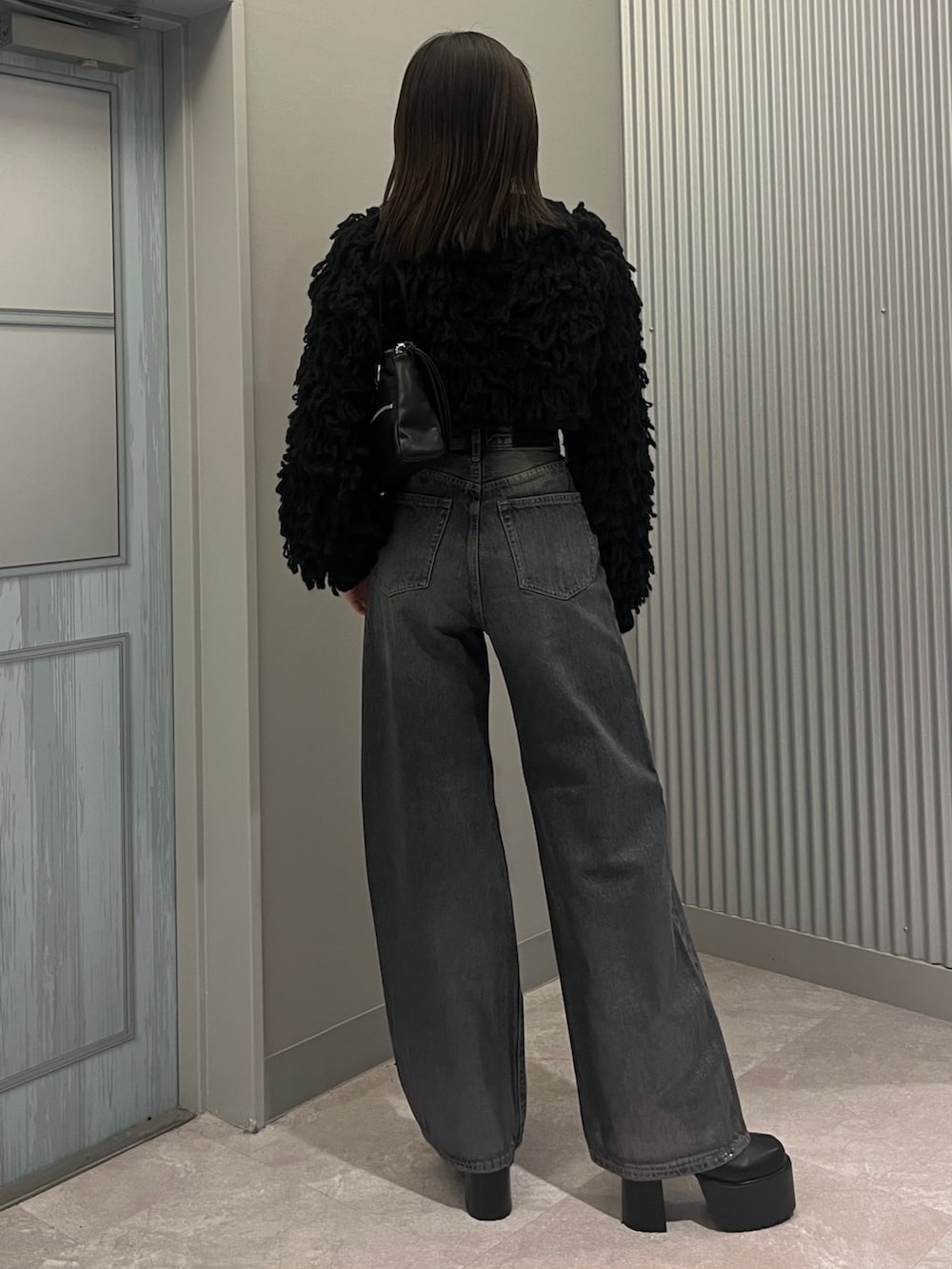 ブルー系のデニムパンツ、ブラック系のニット/セーター、ブラック系のショルダーバッグを着用したレディースの秋コーディネートの3枚目の写真