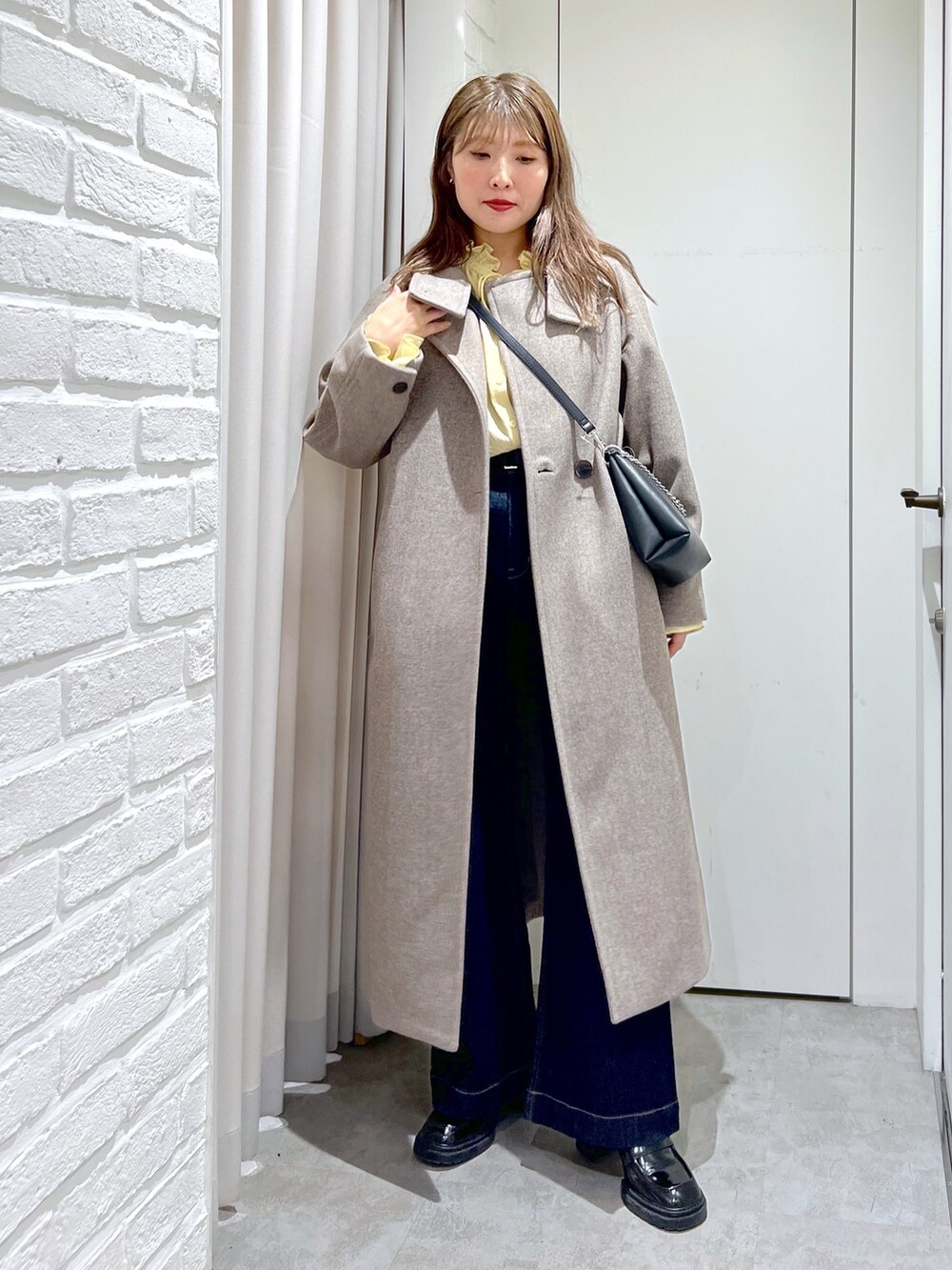 ブラウン系のステンカラーコート、ブラック系のショルダーバッグ、イエロー系のシャツ/ブラウスを着用したレディースの秋コーディネートの3枚目の写真