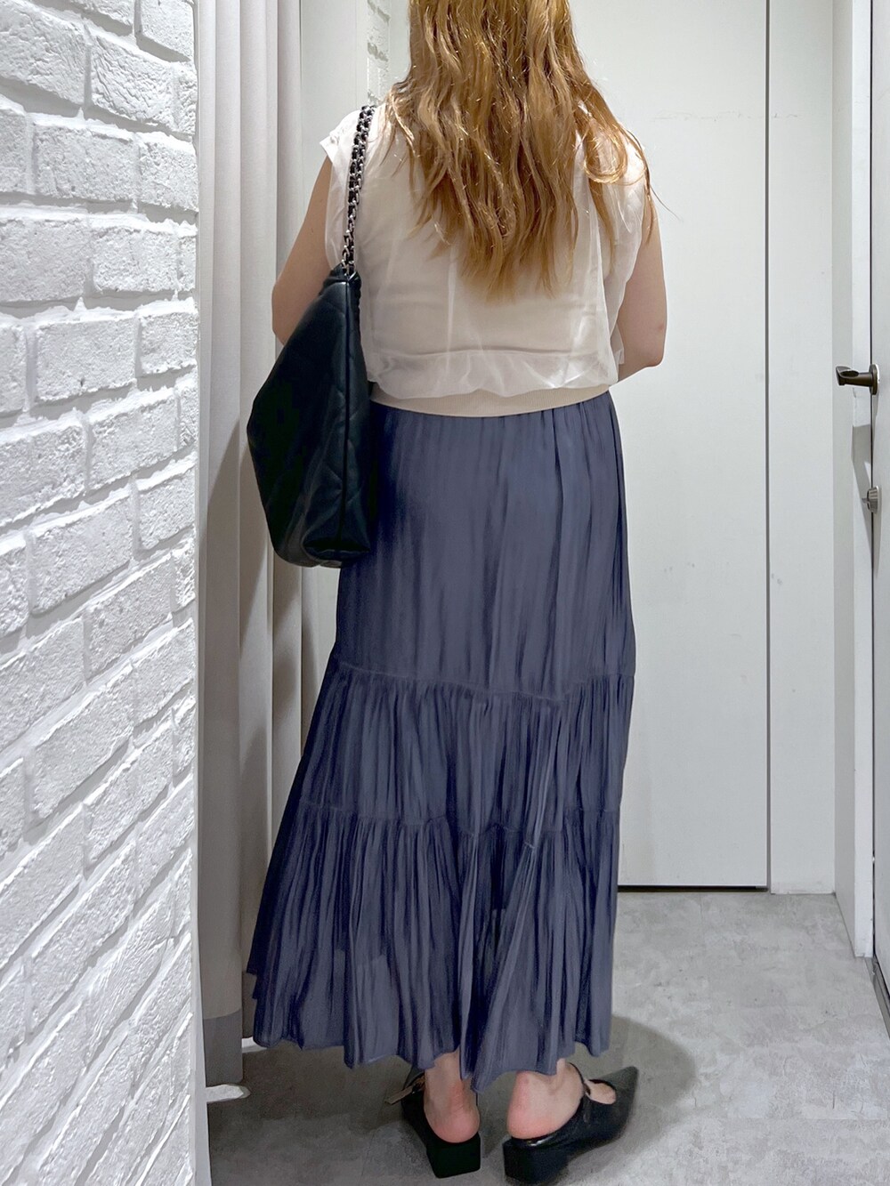 ブルー系のスカート、ホワイト系のベスト、ブラック系のパンプスを着用したレディースの夏コーディネートの5枚目の写真