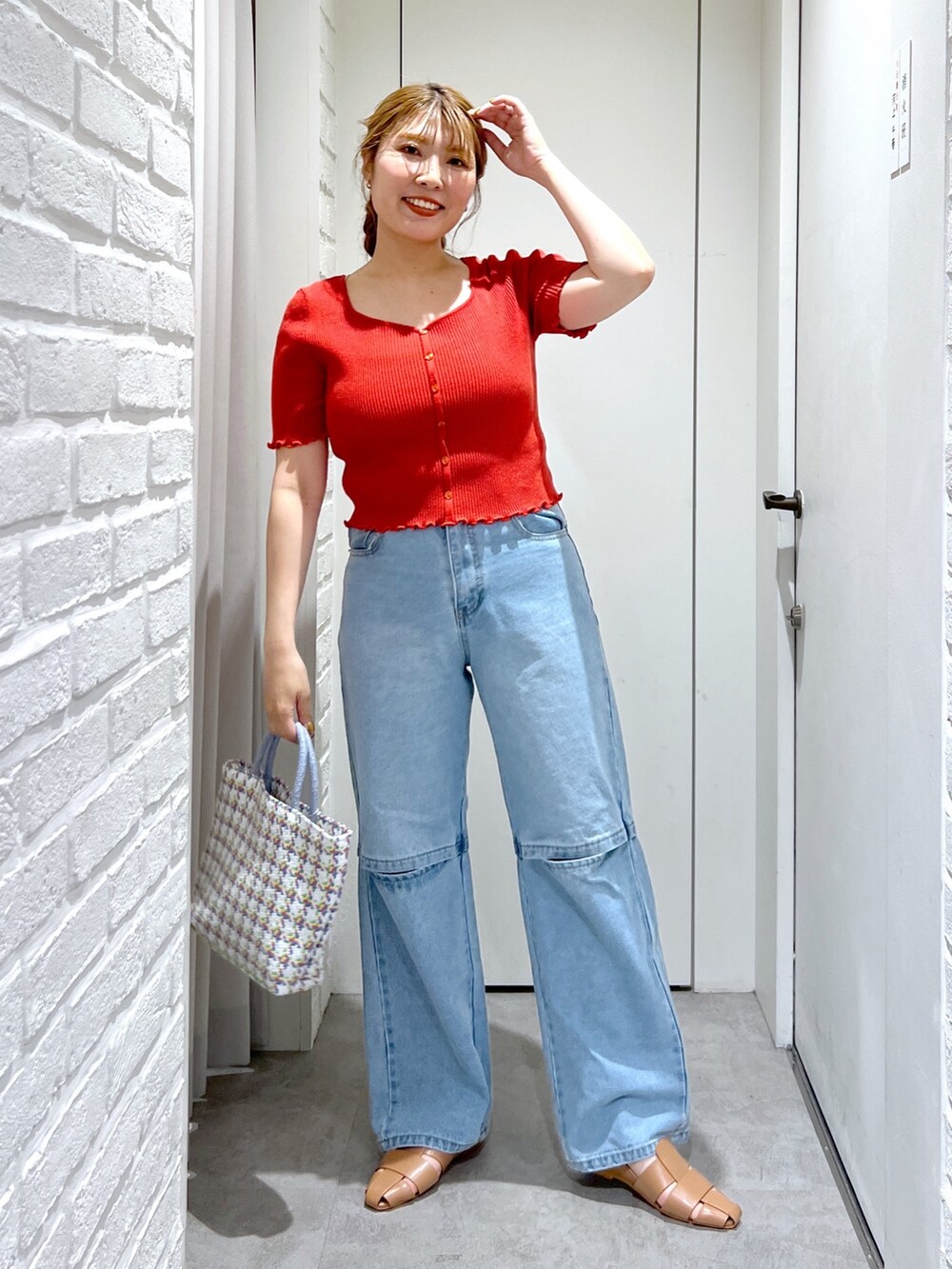 レッド系のニット/セーター、ブルー系のデニムパンツ、ベージュ系のスリッポンを着用したレディースの夏コーディネートの2枚目の写真