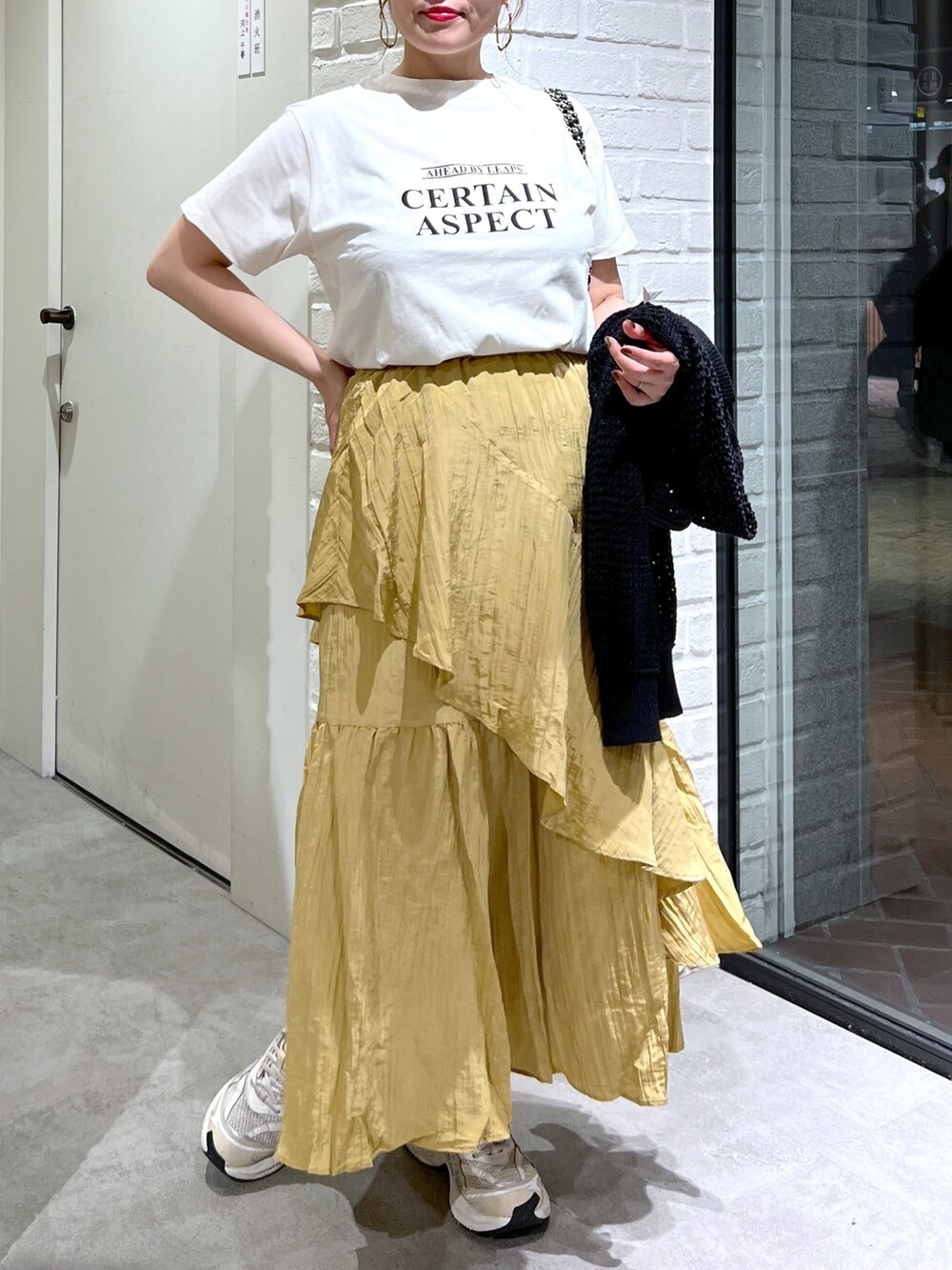 イエロー系のスカート、ブラック系のカーディガン/ボレロ、ホワイト系のTシャツ/カットソーを着用したレディースの夏コーディネートの3枚目の写真