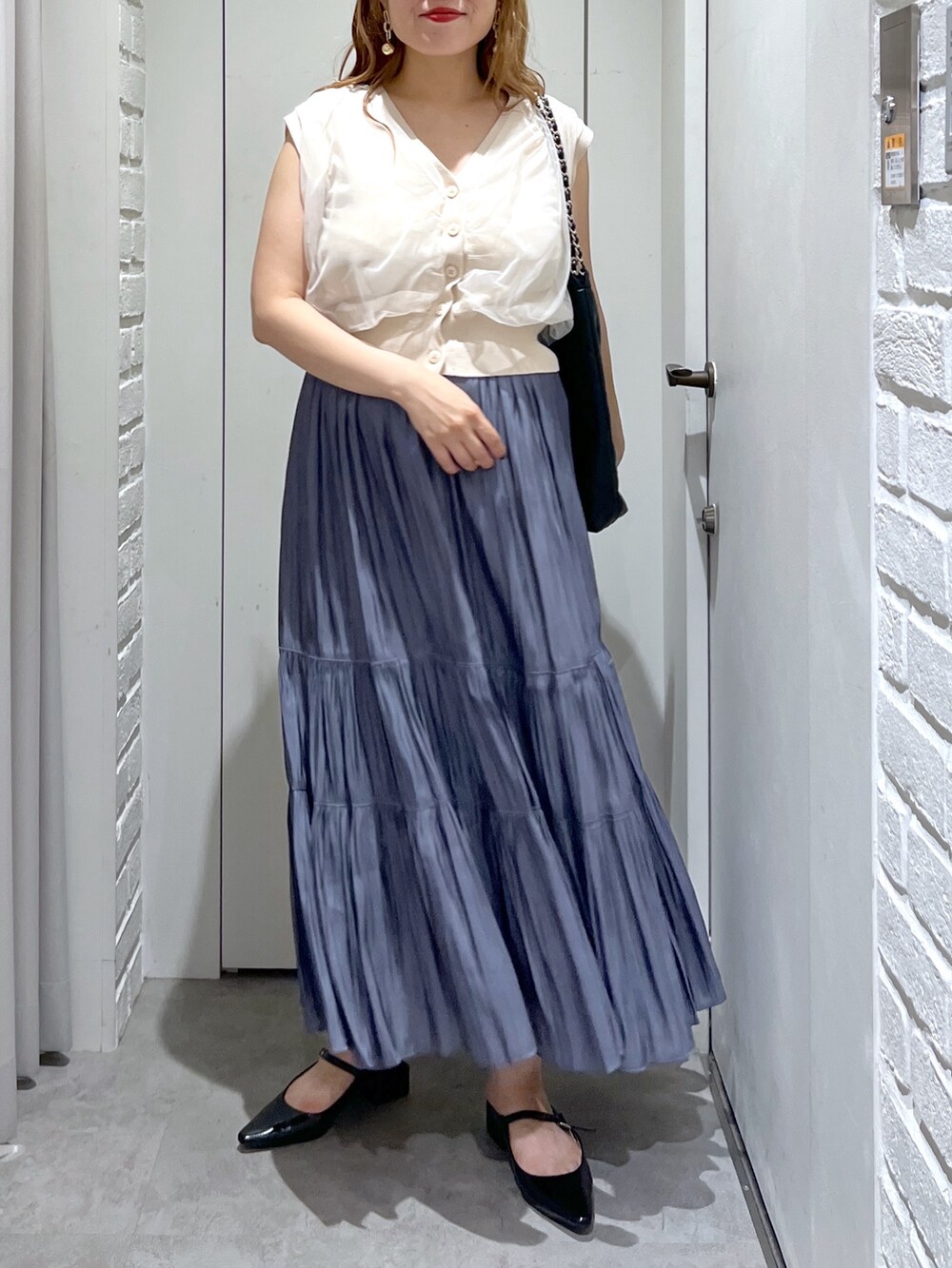 ブルー系のスカート、ホワイト系のベスト、ブラック系のパンプスを着用したレディースの夏コーディネートの3枚目の写真