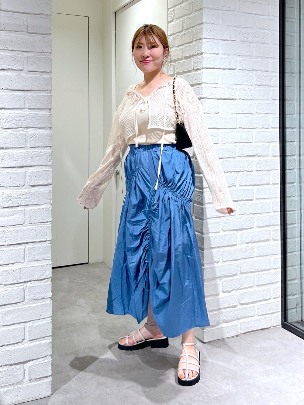 ブルー系のスカート、ホワイト系のカーディガン/ボレロ、ホワイト系のサンダルを着用したレディースの夏コーディネートの2枚目の写真