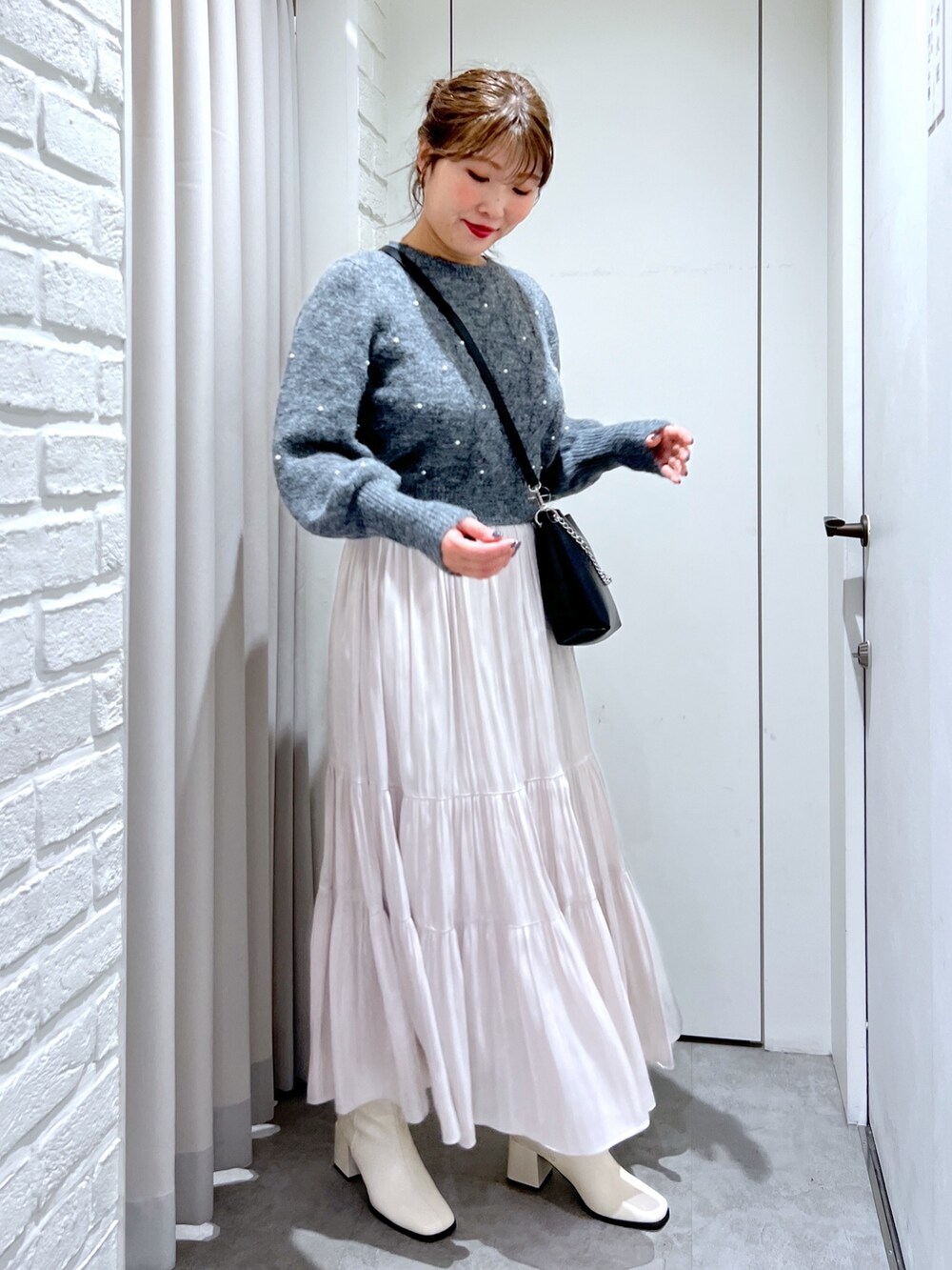 ホワイト系のスカート、グレー系のニット/セーター、ブラック系のショルダーバッグを着用したレディースの冬コーディネートの2枚目の写真