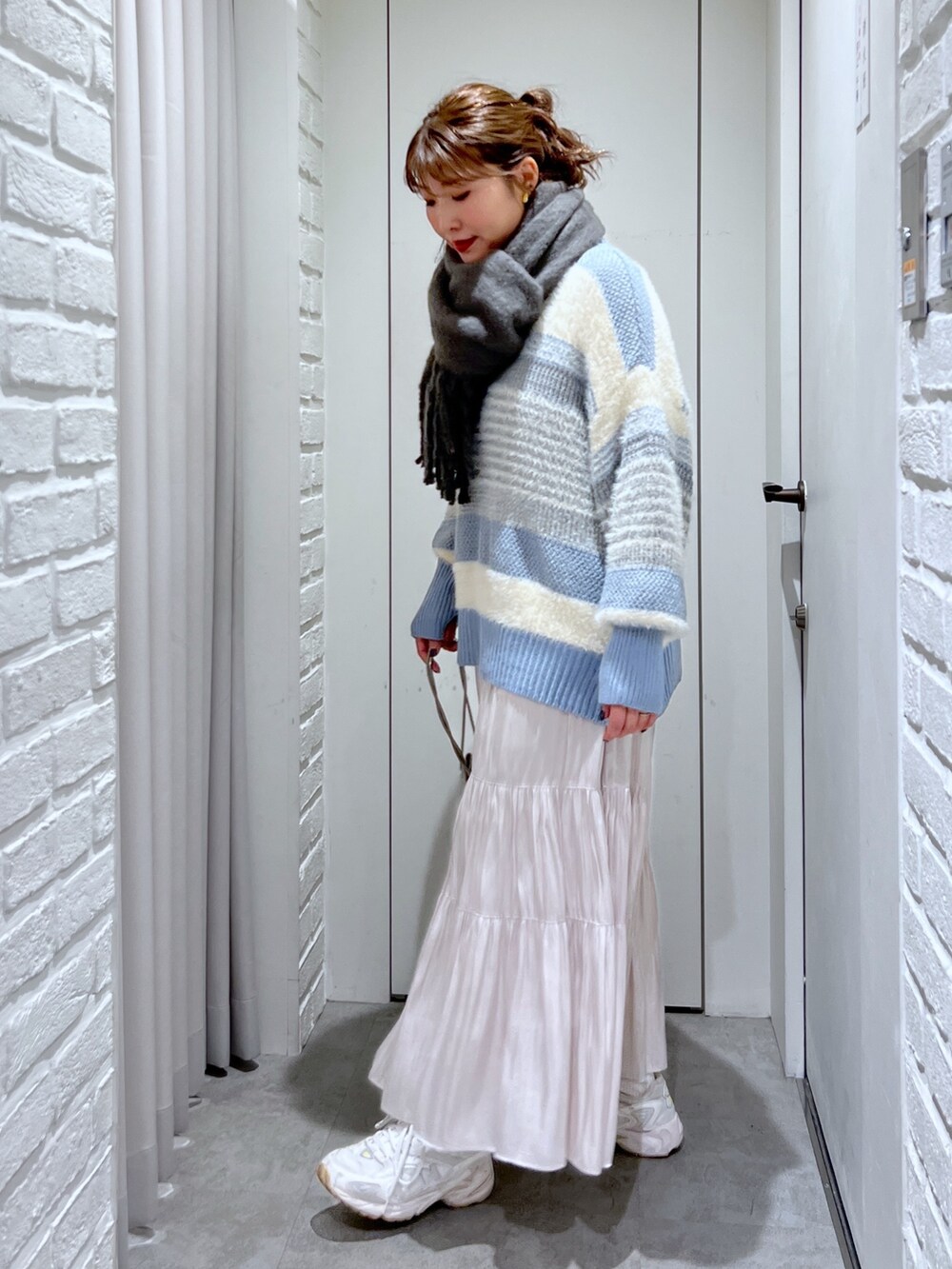 ブルー系のニット/セーター、ホワイト系のスカート、シルバー系のショルダーバッグを着用したレディースの冬コーディネートの2枚目の写真