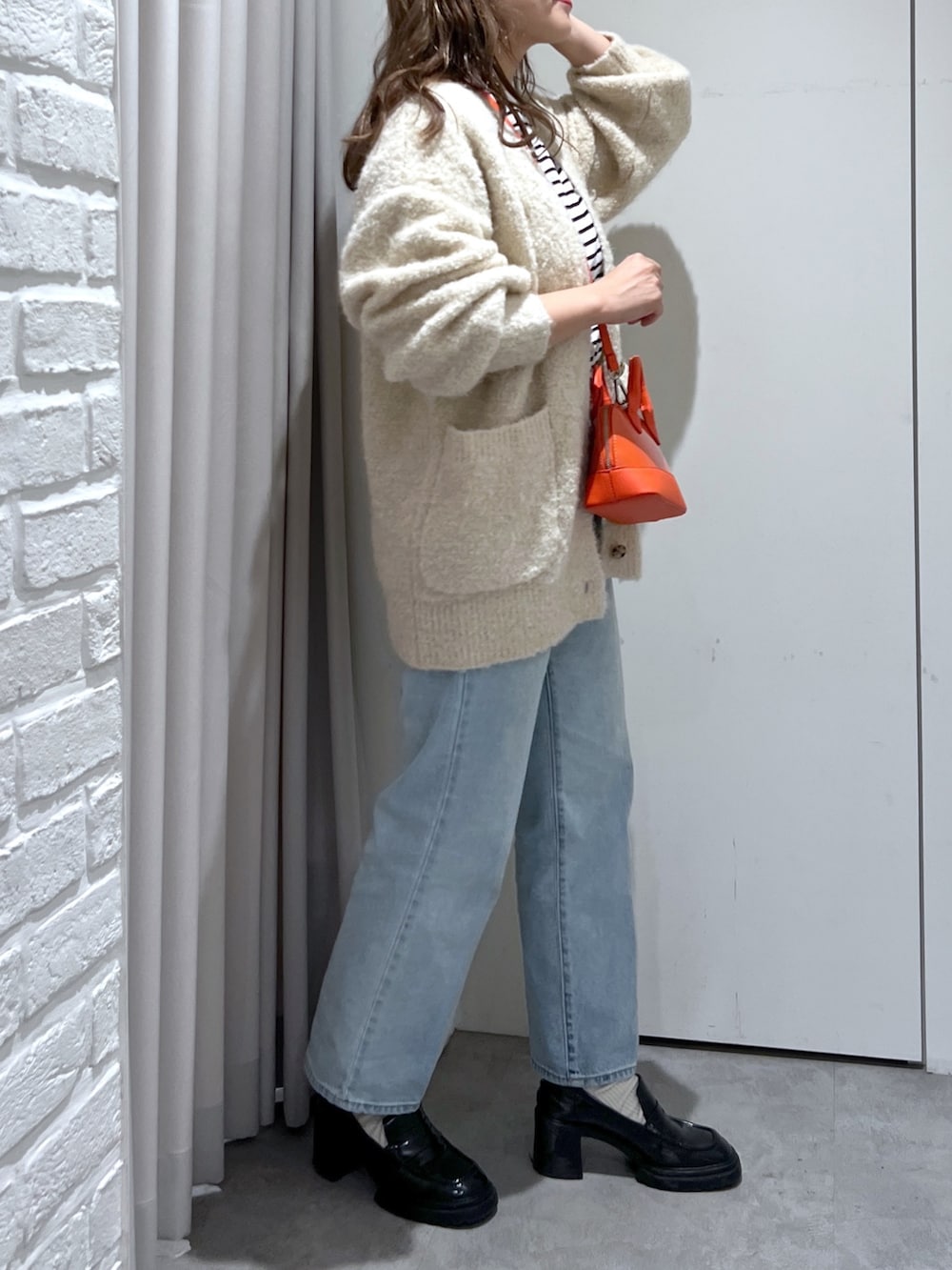 オレンジ系のショルダーバッグ、ブラック系のTシャツ/カットソー、ホワイト系のカーディガン/ボレロを着用したレディースの秋コーディネートの2枚目の写真