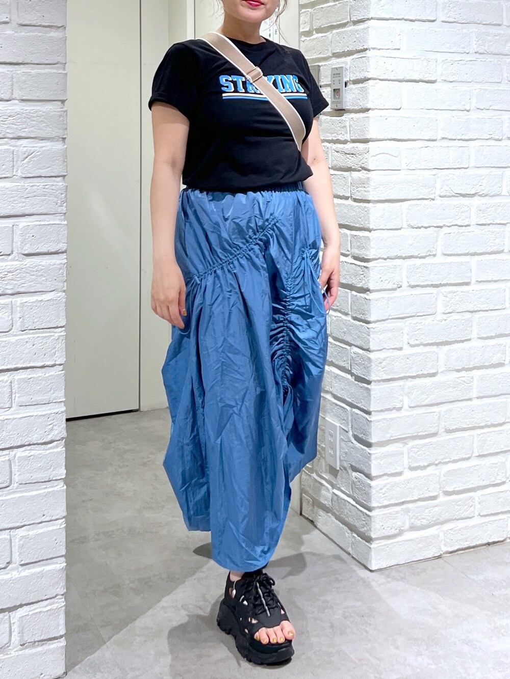 ブルー系のスカート、ブラック系のTシャツ/カットソー、ブラック系のサンダルを着用したレディースの夏コーディネートの3枚目の写真