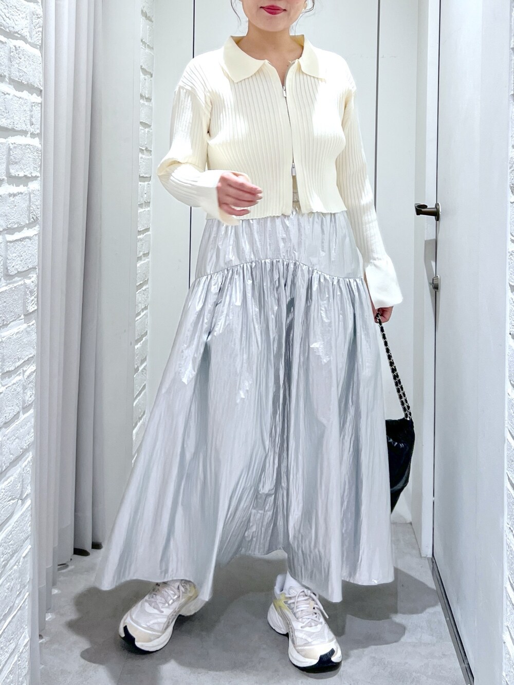 シルバー系のスカート、ホワイト系のニット/セーター、ブラック系のトートバッグを着用したレディースの冬コーディネートの4枚目の写真