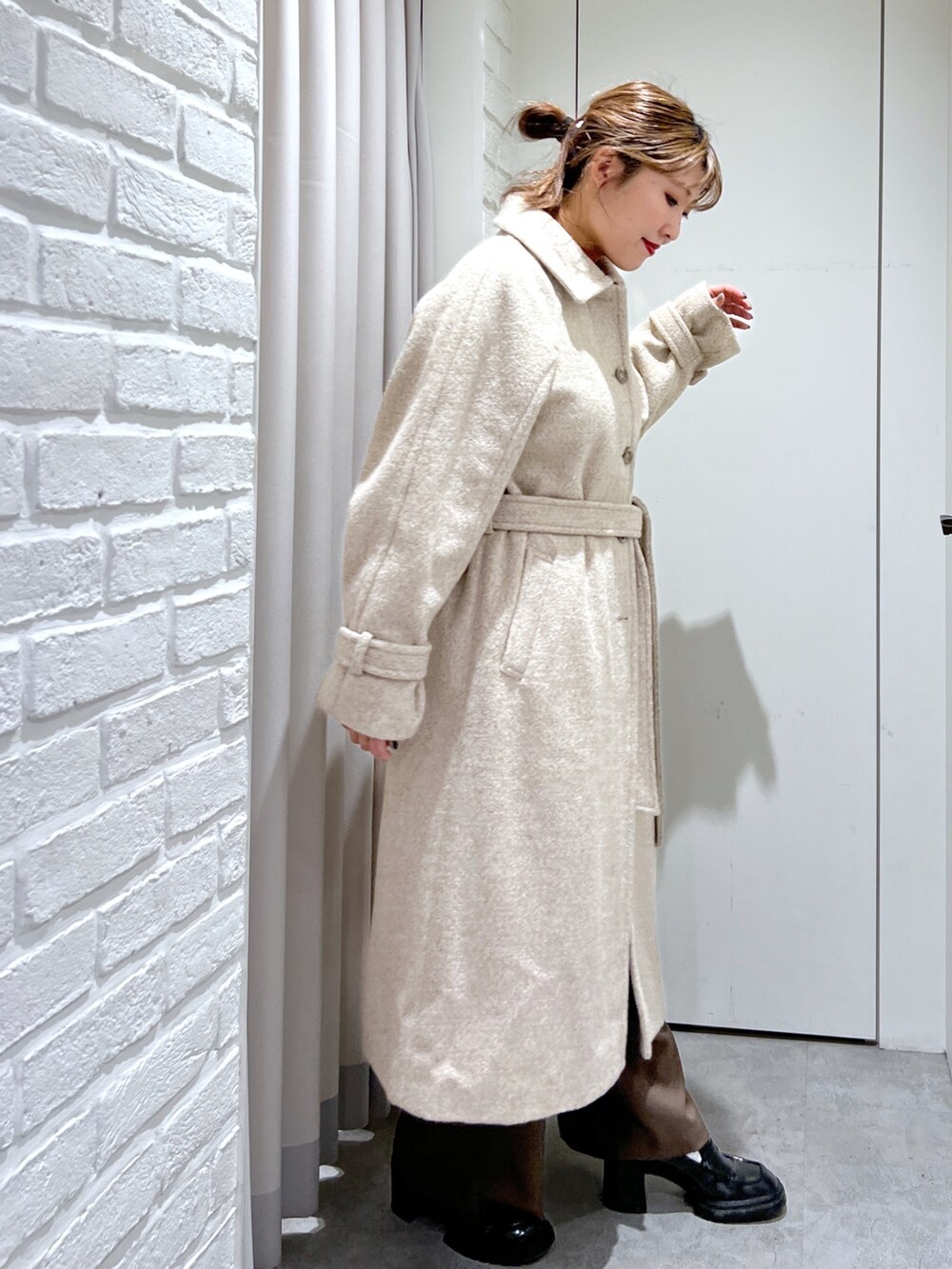 ベージュ系のステンカラーコート、オレンジ系のニット/セーター、ブラウン系のスラックスを着用したレディースの秋コーディネートの5枚目の写真