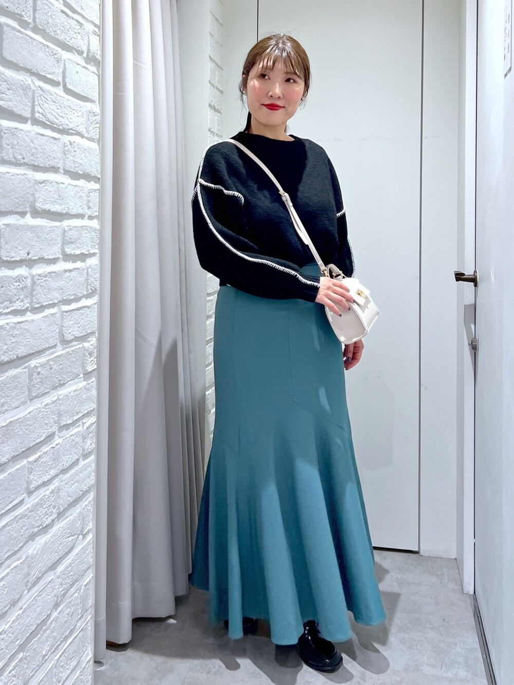 グリーン系のスカート、ブラック系のニット/セーター、ホワイト系のショルダーバッグを着用したレディースの冬コーディネートの2枚目の写真