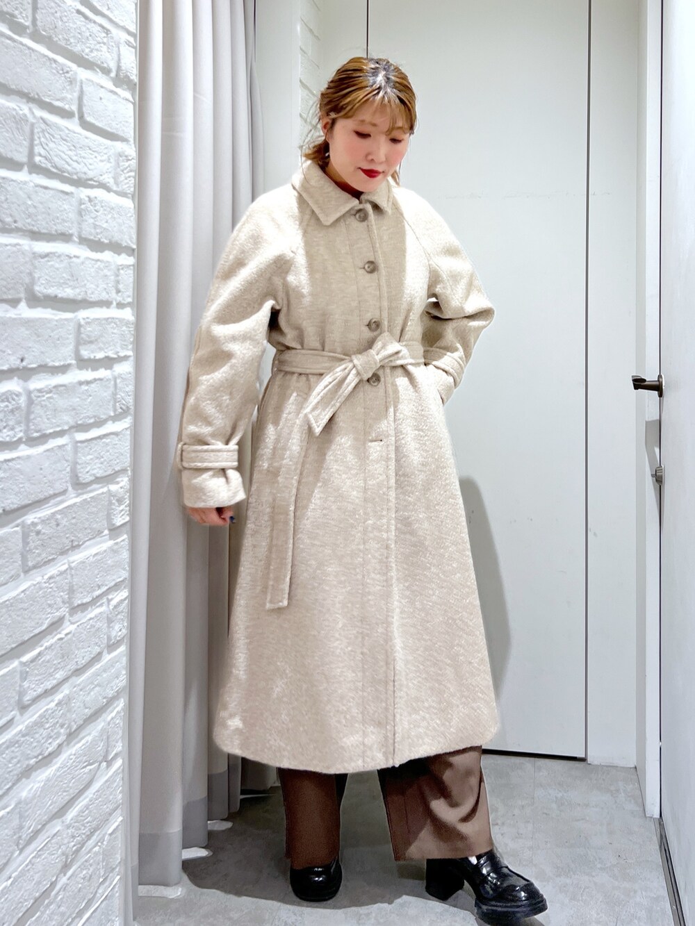 ベージュ系のステンカラーコート、オレンジ系のニット/セーター、ブラウン系のスラックスを着用したレディースの秋コーディネートの2枚目の写真