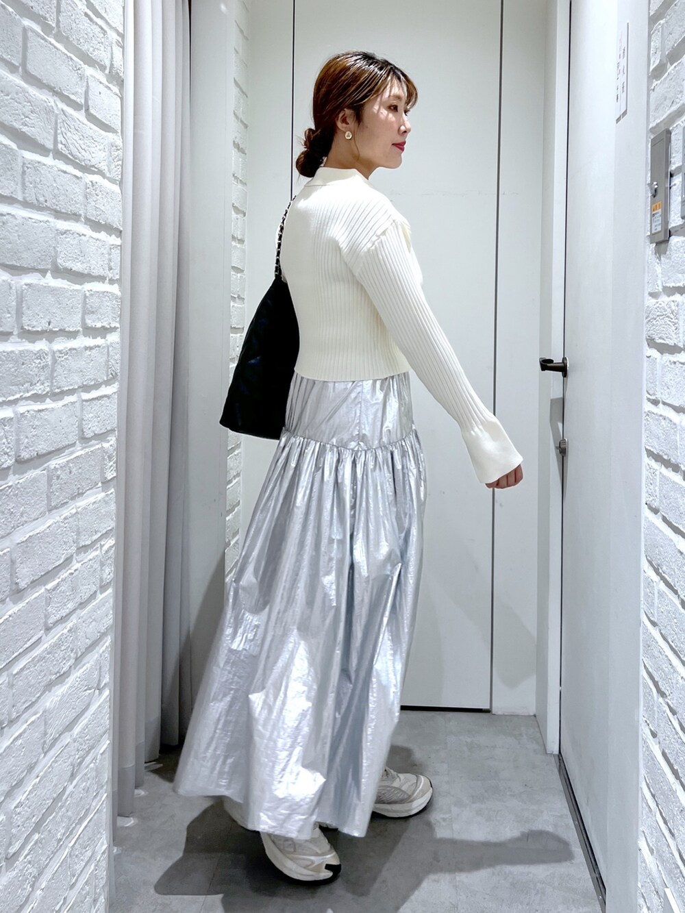 シルバー系のスカート、ホワイト系のニット/セーター、ブラック系のトートバッグを着用したレディースの冬コーディネートの2枚目の写真