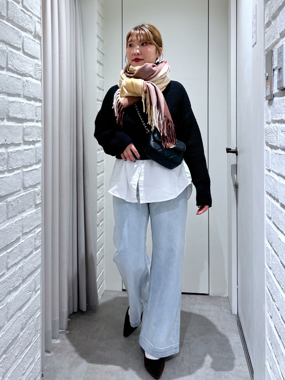 ブルー系のデニムパンツ、ブラック系のショルダーバッグ、ブラック系のニット/セーターを着用したレディースの冬コーディネートの2枚目の写真