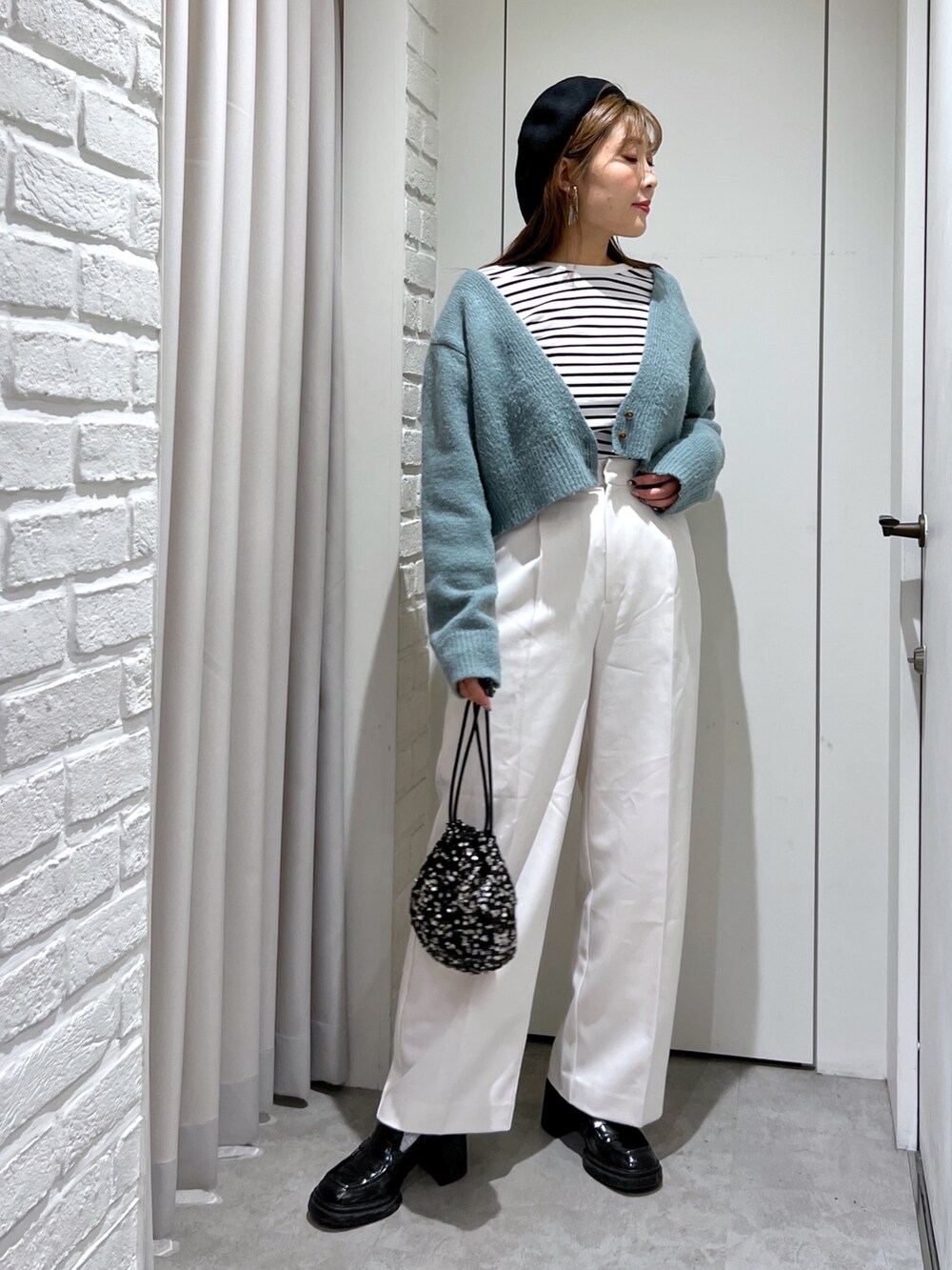 グリーン系のニット/セーター、ブラック系のTシャツ/カットソー、ホワイト系のスラックスを着用したレディースの秋コーディネートの2枚目の写真