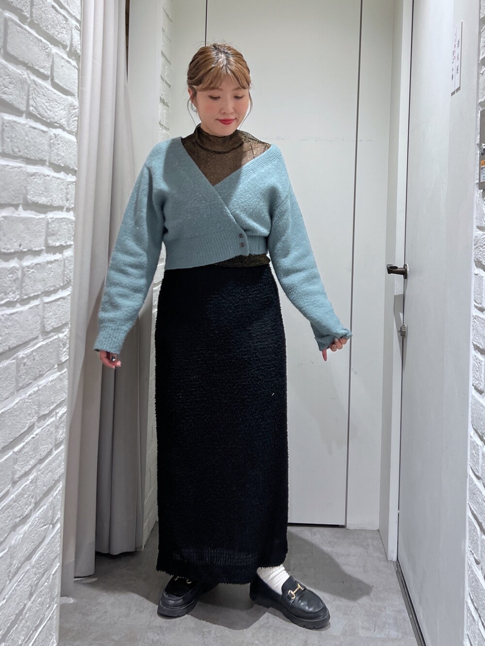 ブラック系のスカート、グリーン系のニット/セーター、ブラック系のTシャツ/カットソーを着用したレディースの秋コーディネートの2枚目の写真