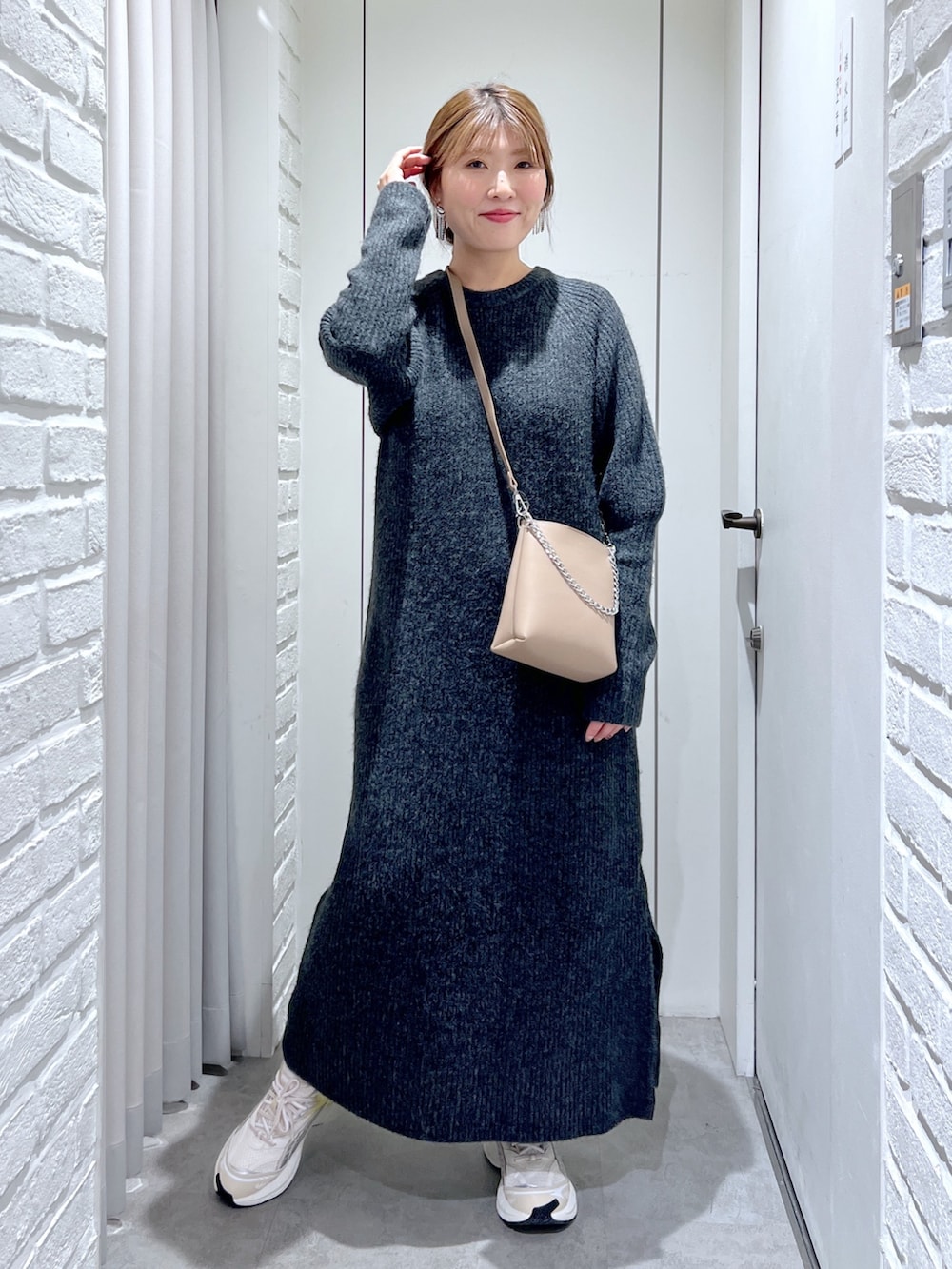 ブラック系のワンピース、ホワイト系のスニーカー、ベージュ系のショルダーバッグを着用したレディースの冬コーディネートの2枚目の写真