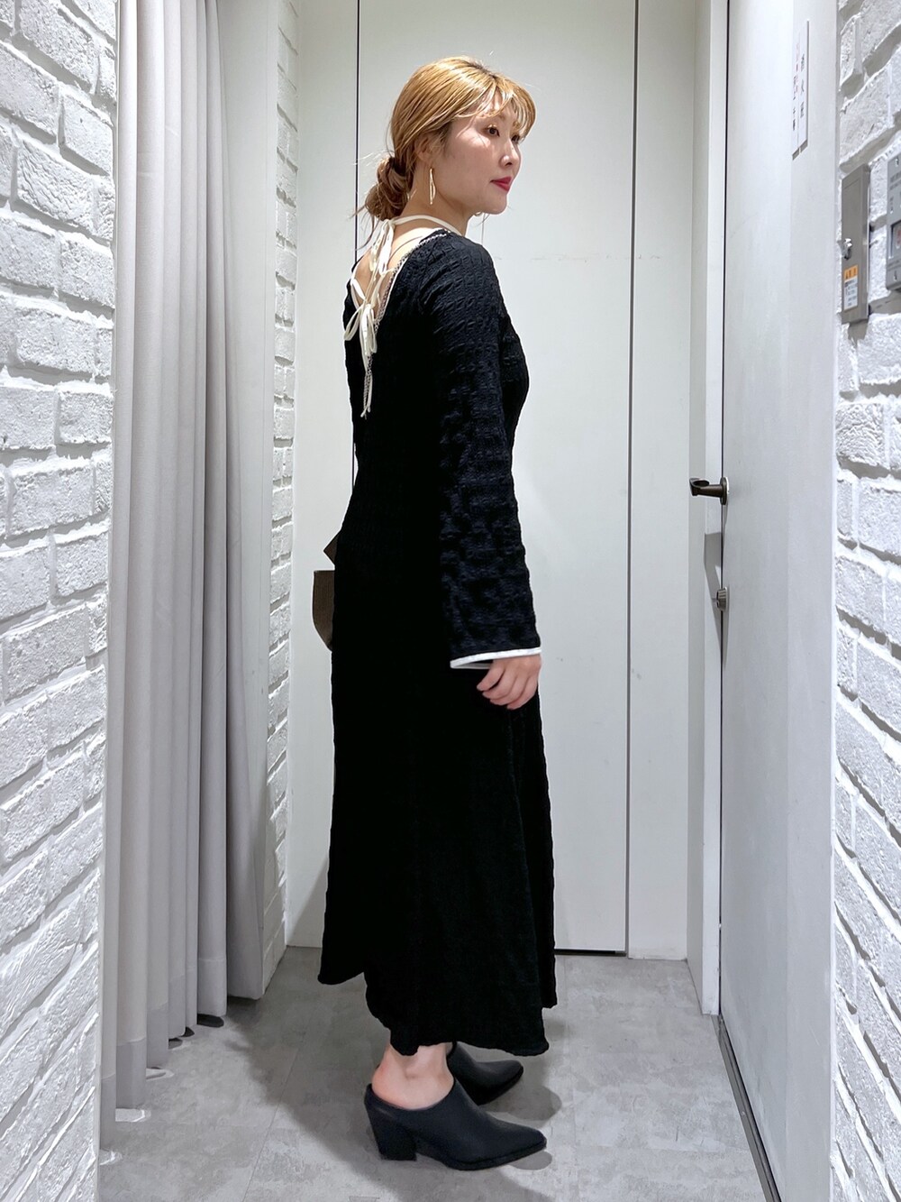 ブラック系のワンピース、ブラック系のパンプス、ゴールド系のショルダーバッグを着用したレディースの春コーディネートの5枚目の写真