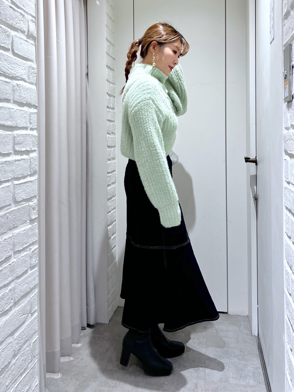 ブルー系のスカート、グリーン系のニット/セーター、シルバー系のショルダーバッグを着用したレディースの冬コーディネートの2枚目の写真