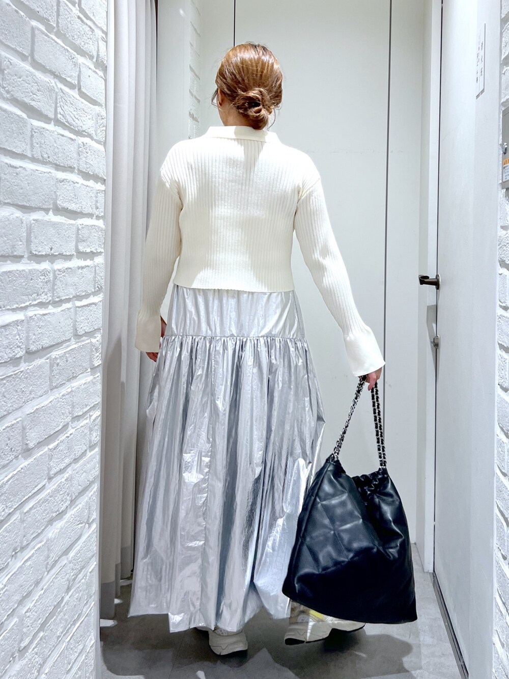シルバー系のスカート、ホワイト系のニット/セーター、ブラック系のトートバッグを着用したレディースの冬コーディネートの3枚目の写真