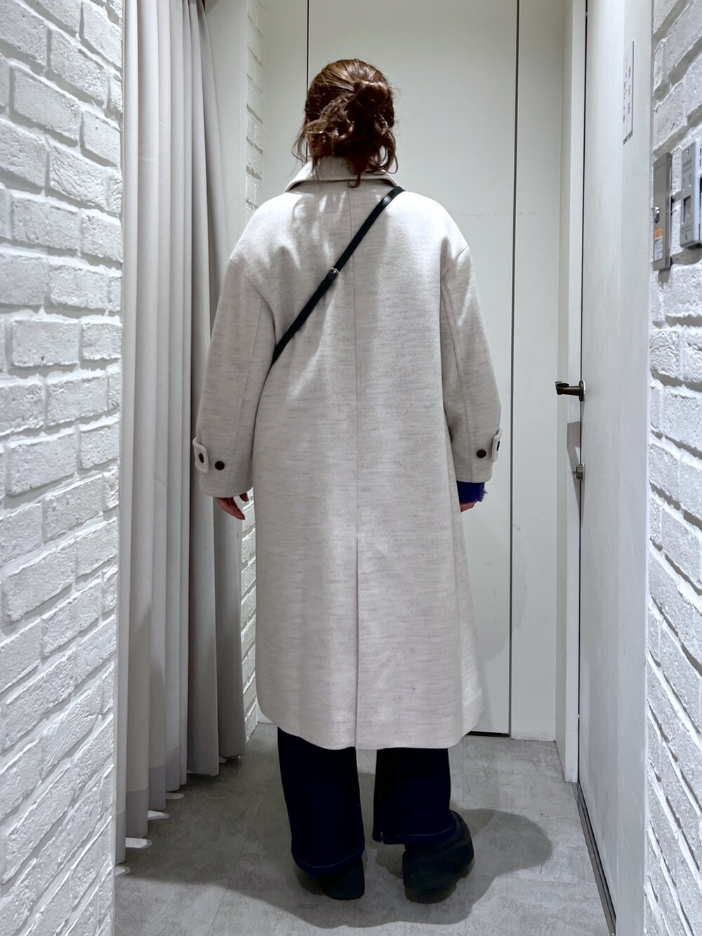 ベージュ系のチェスターコート、ブルー系のデニムパンツ、ブラック系のショルダーバッグを着用したレディースの冬コーディネートの3枚目の写真