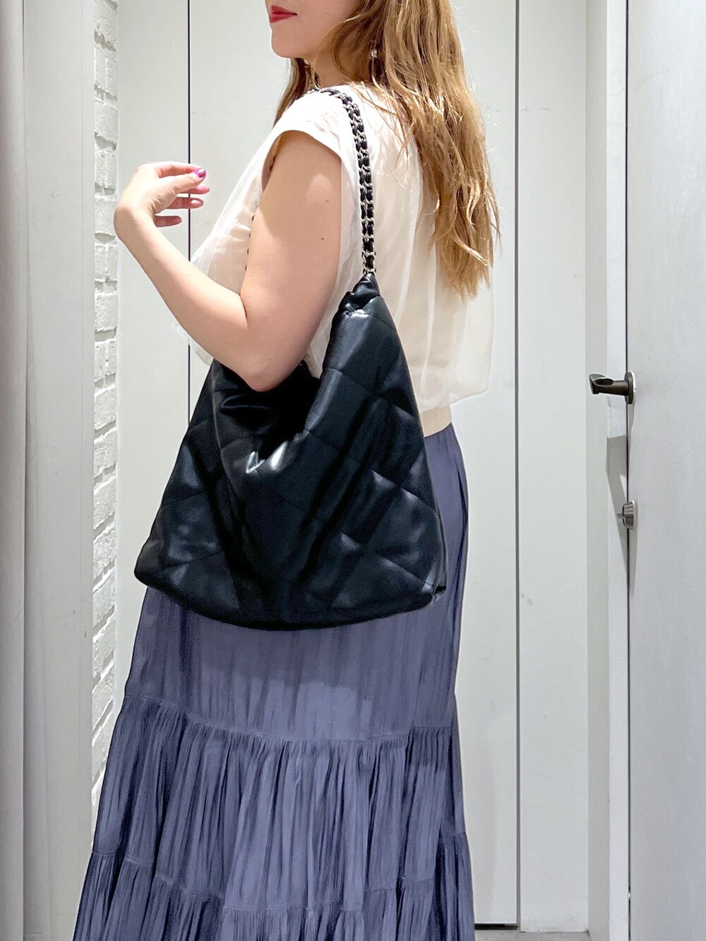 ブルー系のスカート、ホワイト系のベスト、ブラック系のパンプスを着用したレディースの夏コーディネートの6枚目の写真