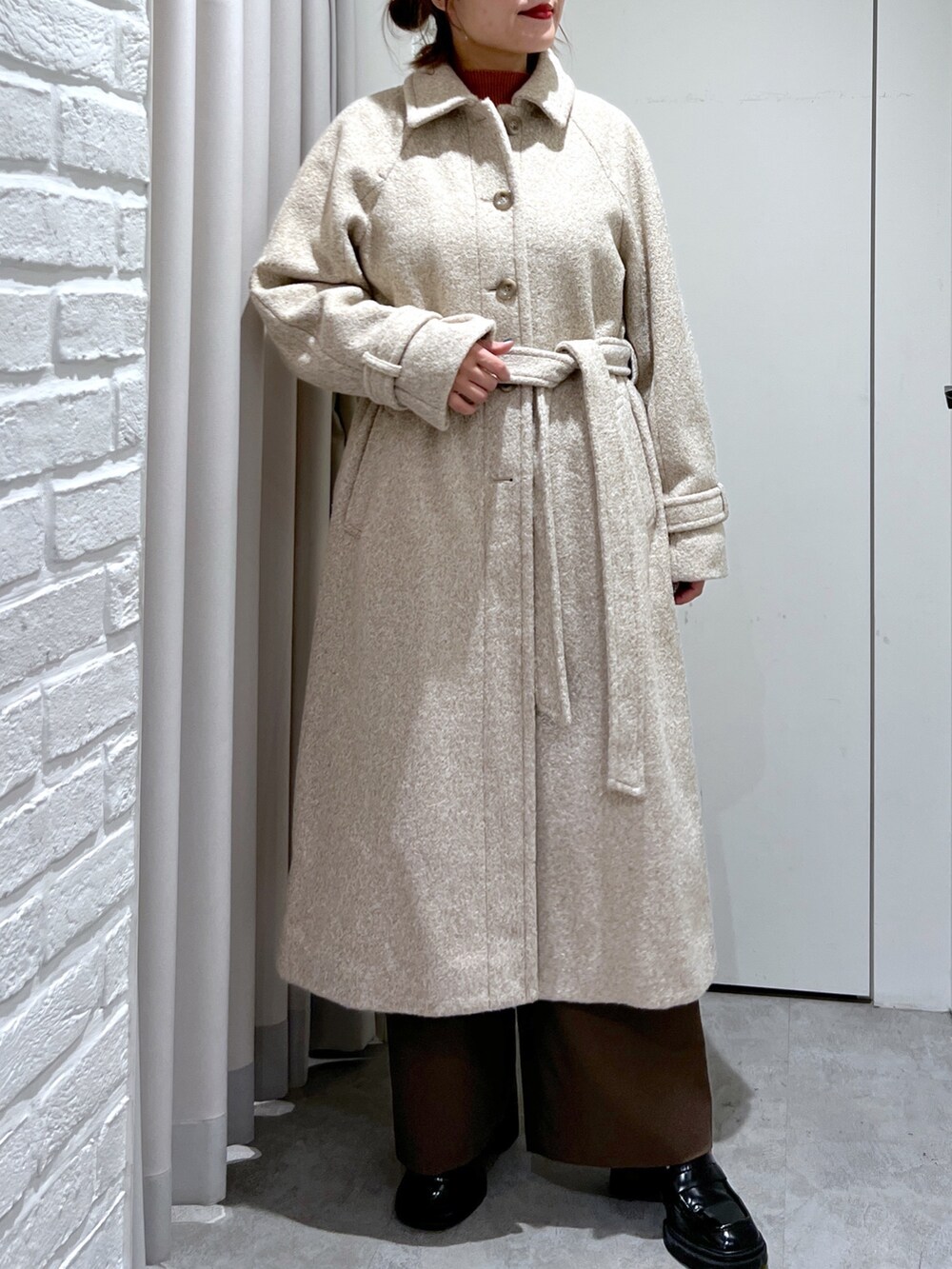 ベージュ系のステンカラーコート、オレンジ系のニット/セーター、ブラウン系のスラックスを着用したレディースの秋コーディネートの4枚目の写真