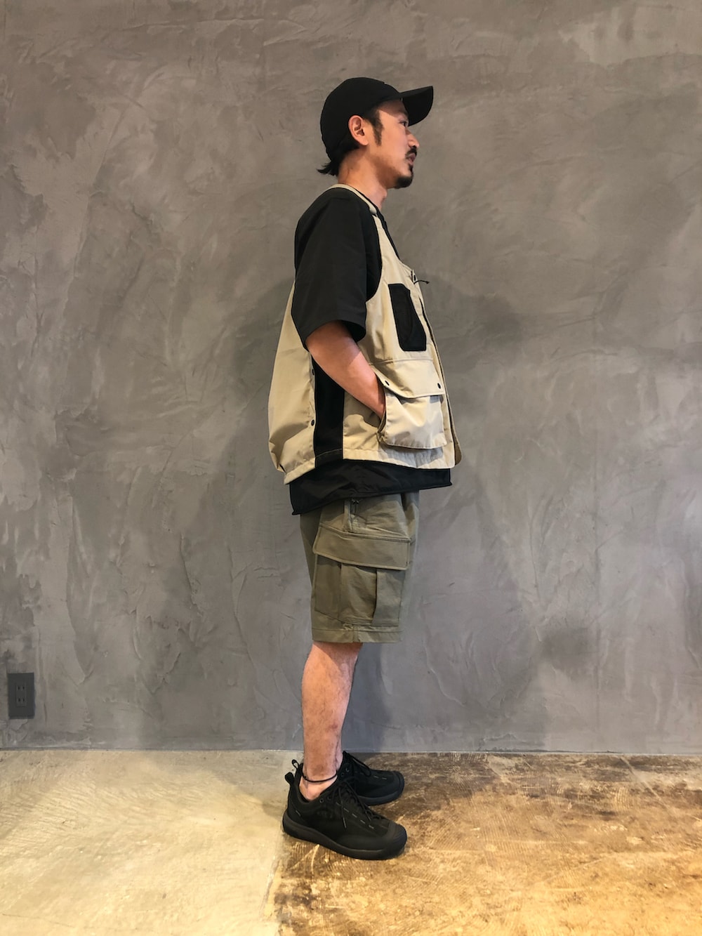 グリーン系のカーゴパンツ、ベージュ系のベスト、ブラック系のTシャツ/カットソーを着用したメンズの春コーディネートの3枚目の写真