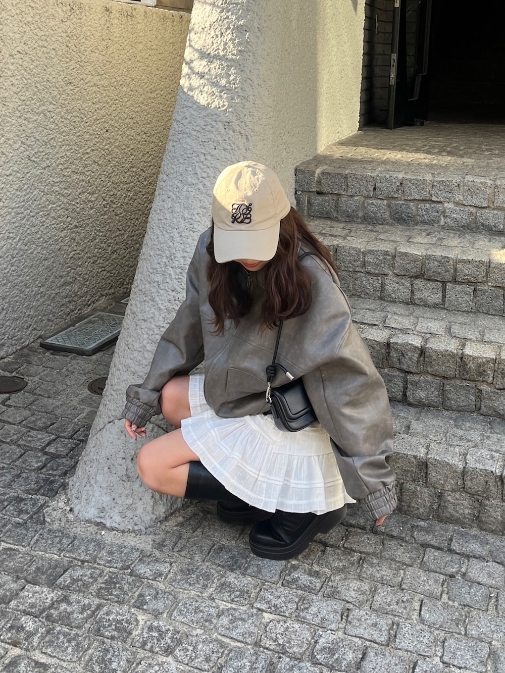 グレー系のライダースジャケット、ホワイト系のスカート、ベージュ系のキャップを着用したレディースの冬コーディネートの4枚目の写真