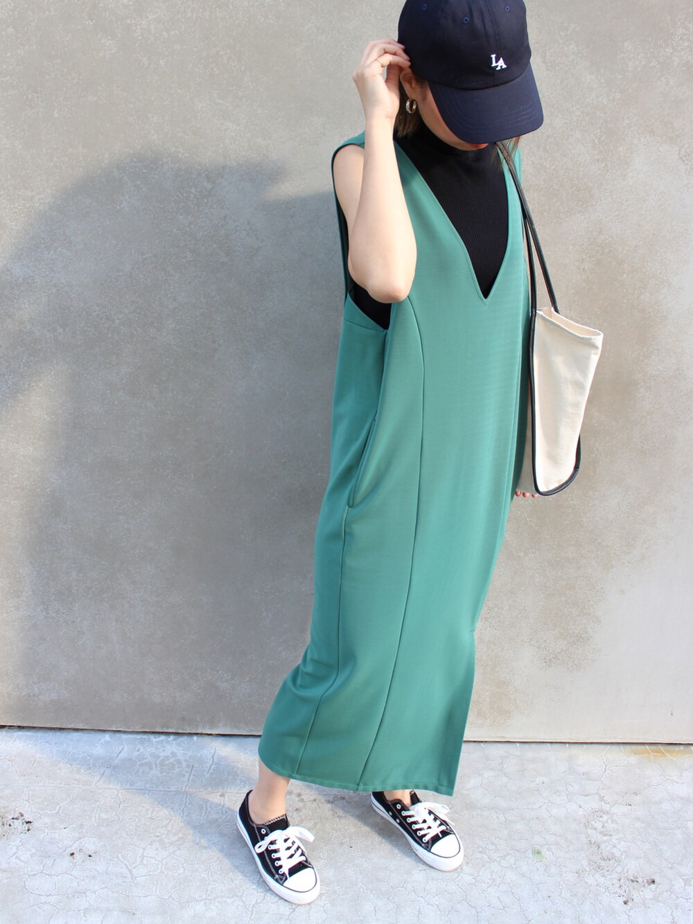 グリーン系のジャンパースカート、ホワイト系のトートバッグ、ベージュ系のキャップを着用したレディースの春コーディネートの2枚目の写真