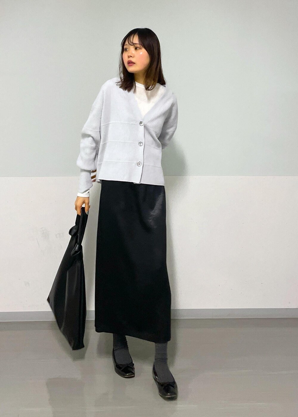 ブラック系のトートバッグ、ホワイト系のTシャツ/カットソー、グレー系のカーディガン/ボレロを着用したレディースの冬コーディネートの2枚目の写真