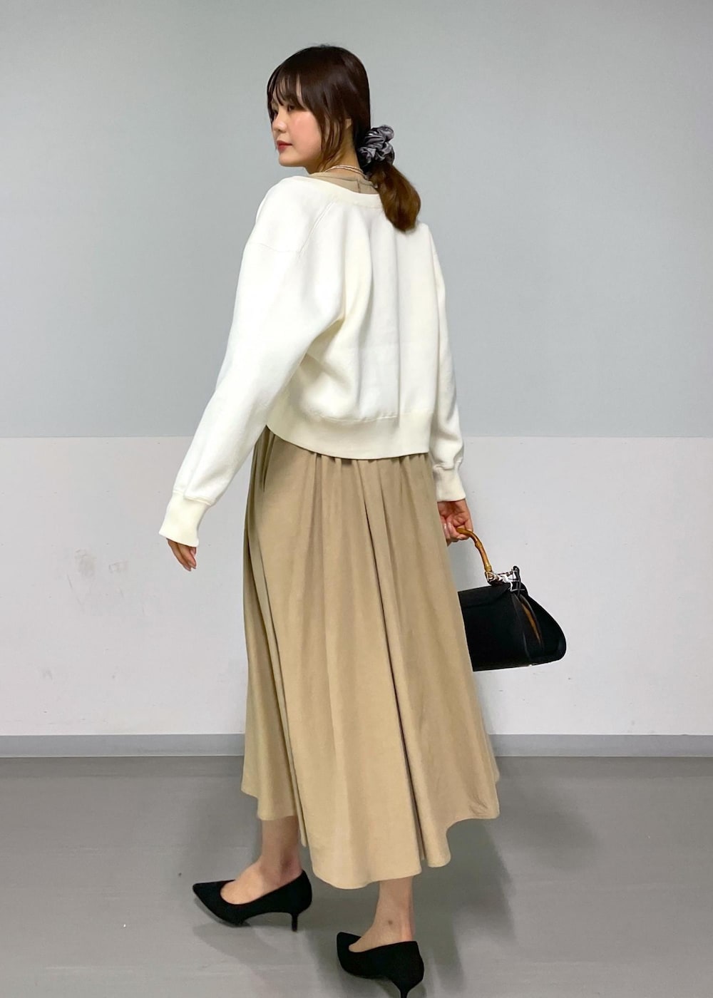 ブラック系のショルダーバッグ、ベージュ系のワンピース、ホワイト系のカーディガン/ボレロを着用したレディースの春コーディネートの5枚目の写真