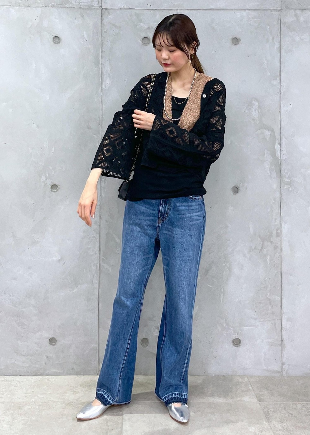 ブラック系のショルダーバッグ、ブルー系のデニムパンツ、ゴールド系のベストを着用したレディースの春コーディネートの3枚目の写真