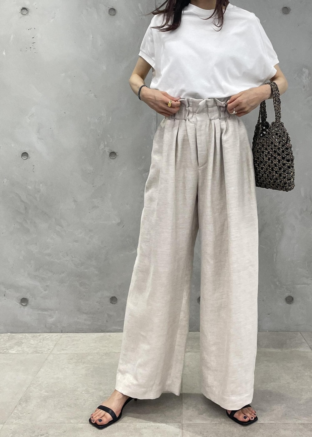 ブラック系のサンダル、ホワイト系のスラックス、ブラック系のハンドバッグを着用したレディースの春コーディネートの2枚目の写真