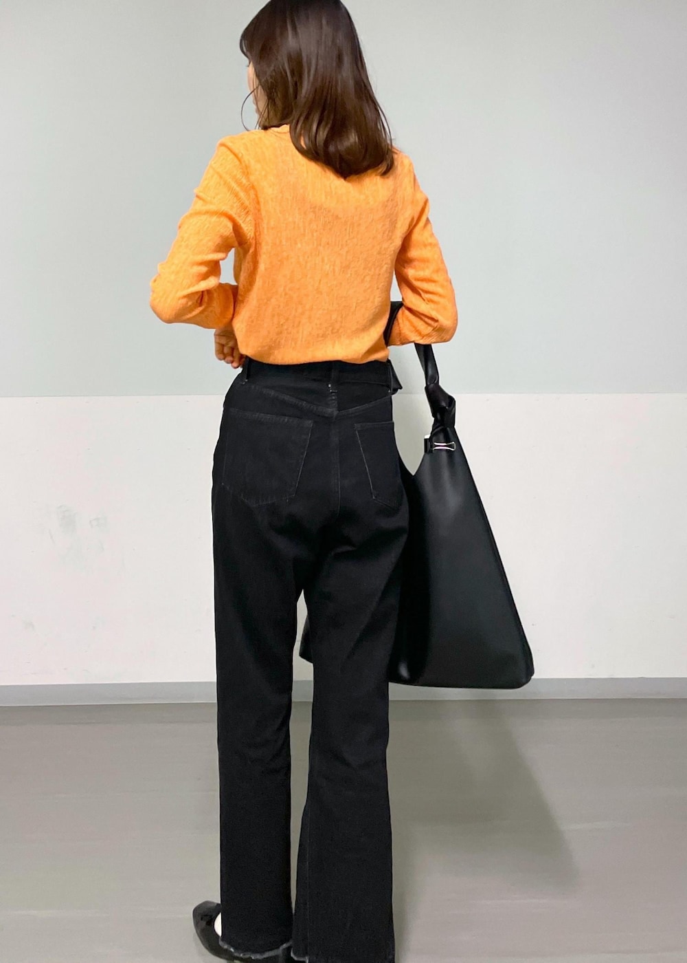 ブラック系のトートバッグ、グレー系のデニムパンツ、オレンジ系のTシャツ/カットソーを着用したレディースの冬コーディネートの2枚目の写真