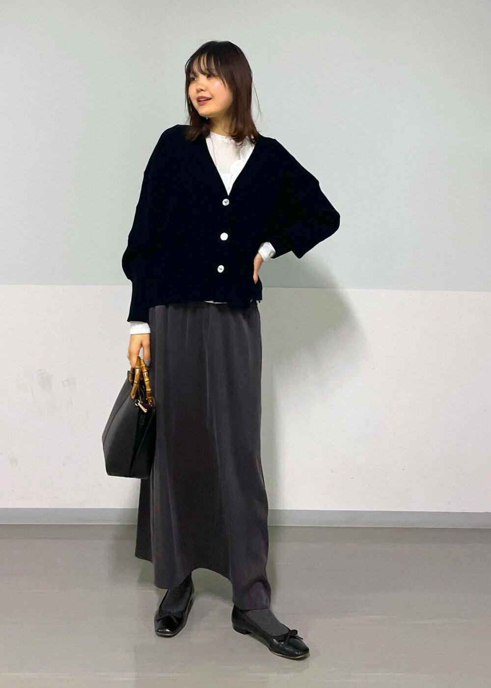 グレー系のスカート、ブラック系のカーディガン/ボレロ、ホワイト系のTシャツ/カットソーを着用したレディースの冬コーディネートの2枚目の写真