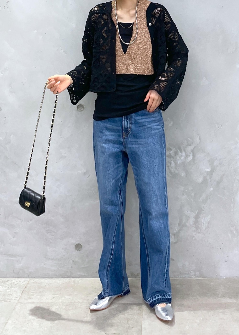 ブラック系のショルダーバッグ、ブルー系のデニムパンツ、ゴールド系のベストを着用したレディースの春コーディネートの6枚目の写真